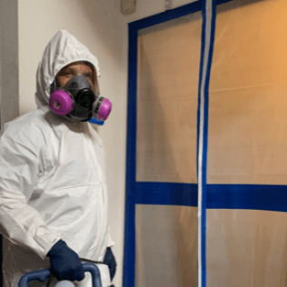 A man wearing a protective suit and mask is standing in a room.
