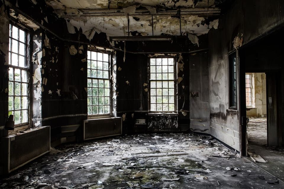 An abandoned room with a lot of windows and a lot of trash on the floor.