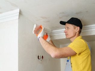 Technician in work gloves inspecting a water-stained ceiling and crown molding.