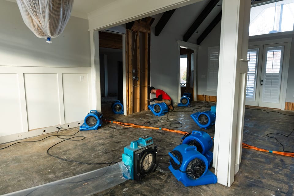 Air movers and a dehumidifier drying a room after the wet flooring was pulled up.